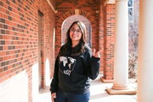 Anne stands under an archway, holding up the "guns-up" sign.